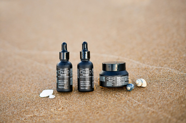 dwie czarne buteleczki i słoiczek z kosmetykami na tle plaży