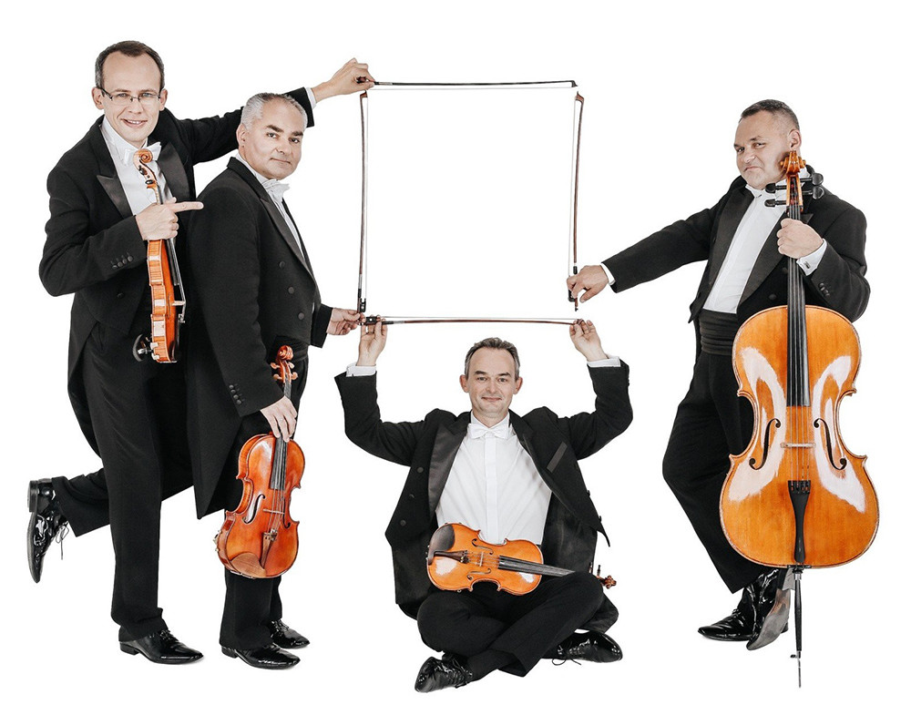 na białym tle: czterech mężczyzn ubranych w czarne eleganckie fraki, białe koszule i białe muszki, w dłoniach trzymają instrumenty: jeden wiolonczelę, a pozostałych trzech trzyma skrzypce, jeden z nich siedzi na podłodze