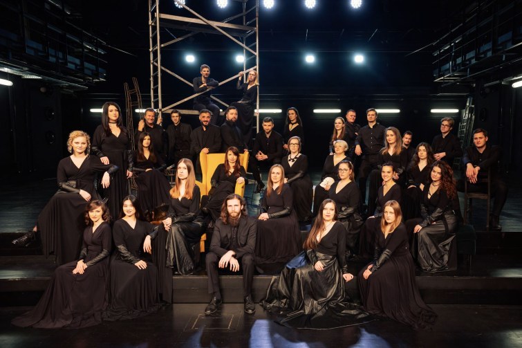 chór: grupa kobiet i mężczyzn ubranych w czarne stoje pozująca do zdjęcia grupowego na scenie