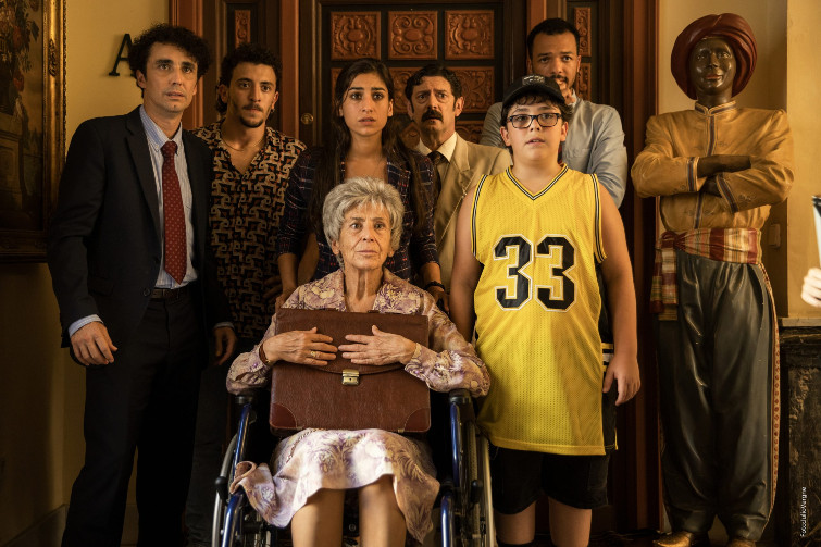 Fotograma de la película, un grupo de personas paradas una al lado de la otra, viejos y jóvenes, pero una de ellas está sentada en una silla de ruedas para personas con discapacidad