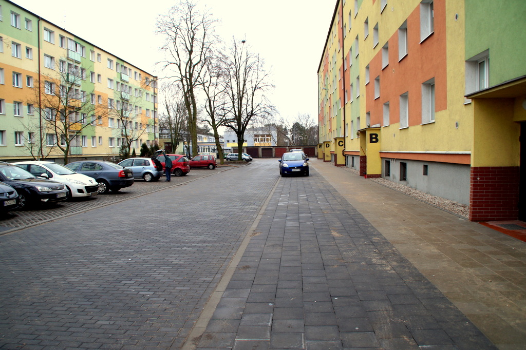 widok na utwardzoną drogę dojazdową, chodnik, wydzielone miejsca parkingowe i zaparkowane samochody