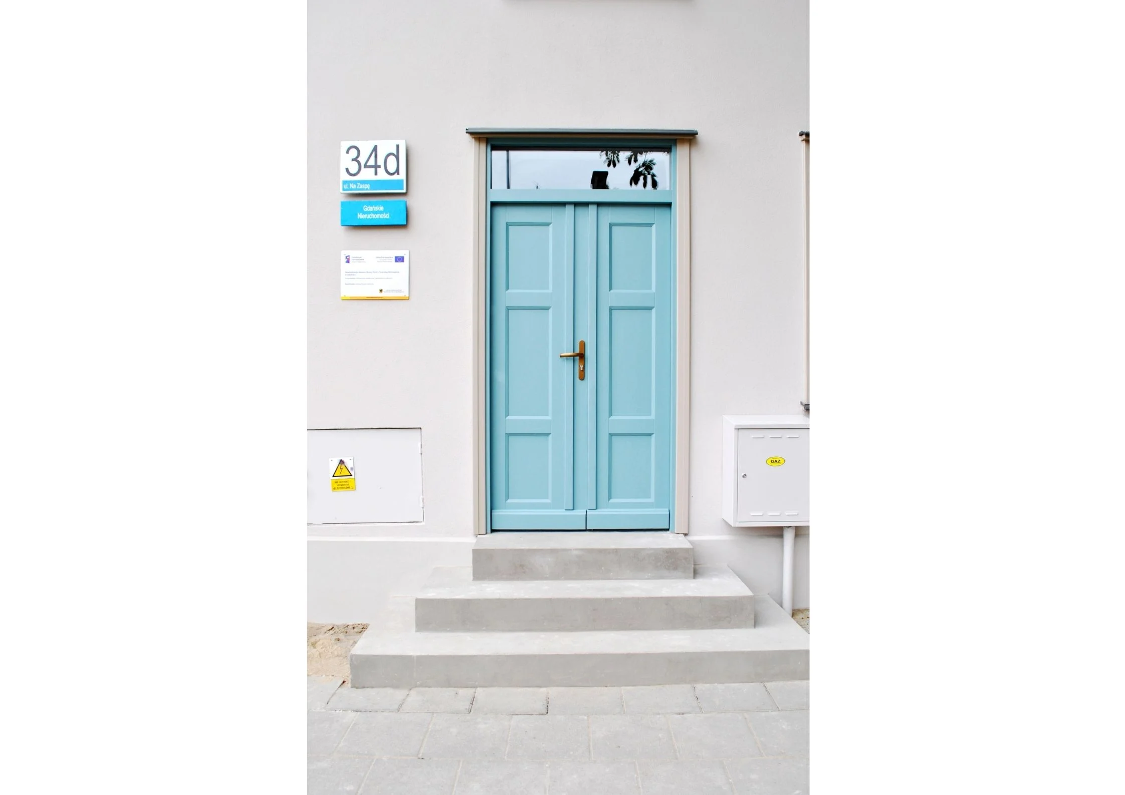Widok wyremontowanego wejścia do budynku z drewnianą stolarką drzwiową w kolorze turkusowym.
