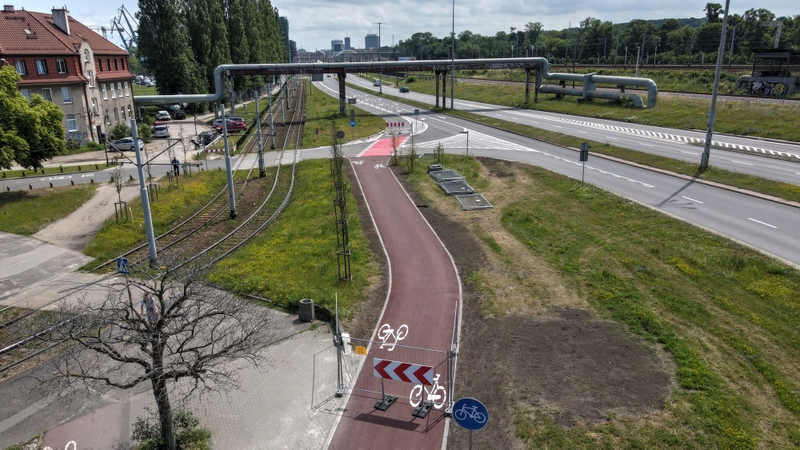 Na zdjęciu widać ścieżkę rowerową, po lewo tory kolejowe, po prawo dwie jezdnie