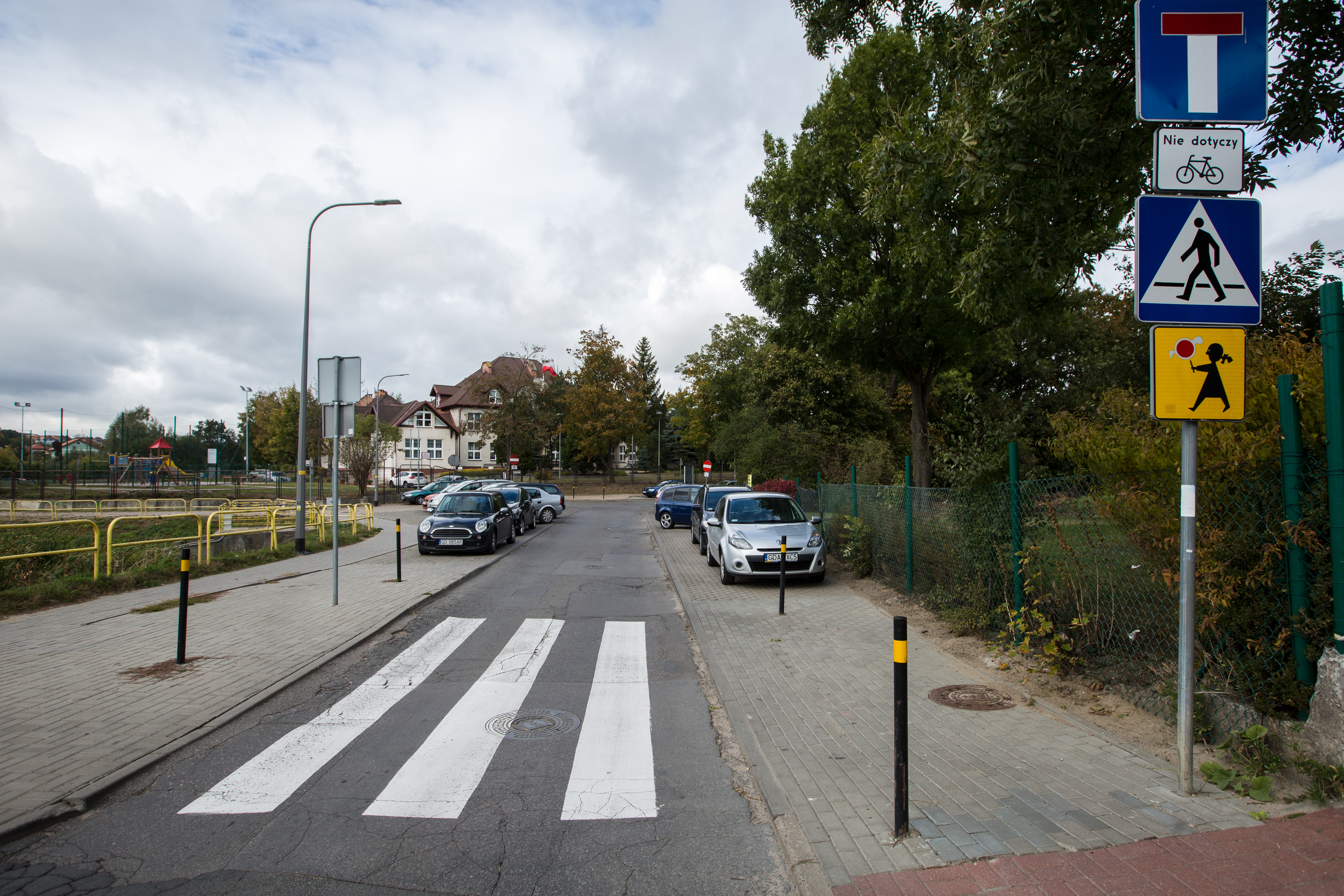 widok na ulicę z wyznaczonym przejściem dla pieszych oraz chodnik po obu stronach drogi z wydzielonymi miejscami parkingowymi