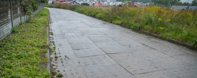 widok na wykonany chodnik w koło zieleń, betonowy płot w oddali zabudowania