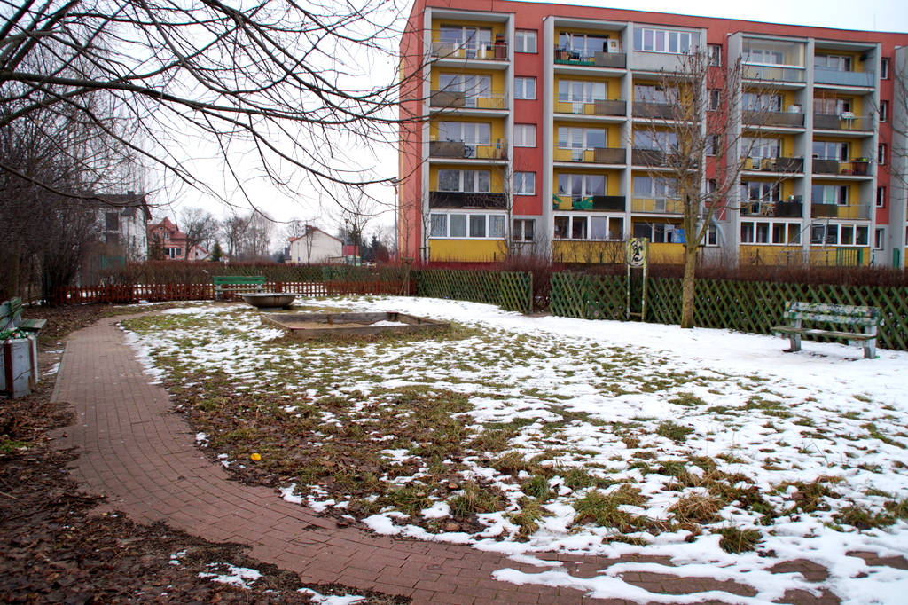 widok na plac zanaw przed modernizacją, poiaskownica, miejscami pokryty śniegiem, w oddali widoczne bloki