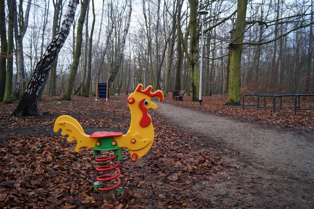 zabawowa bujawka w kształcie koguta w parku na tle drzew jesienną porą