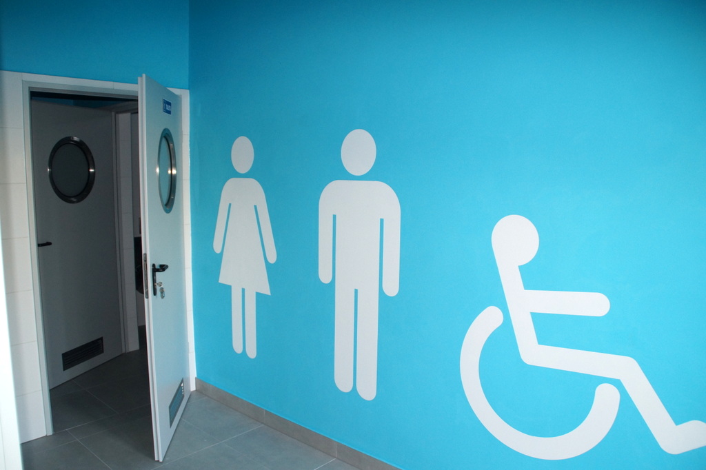 widok wewnątrz budynku toalety, niebieska ściana z oznaczeniami  pomiesazczeń toalet 