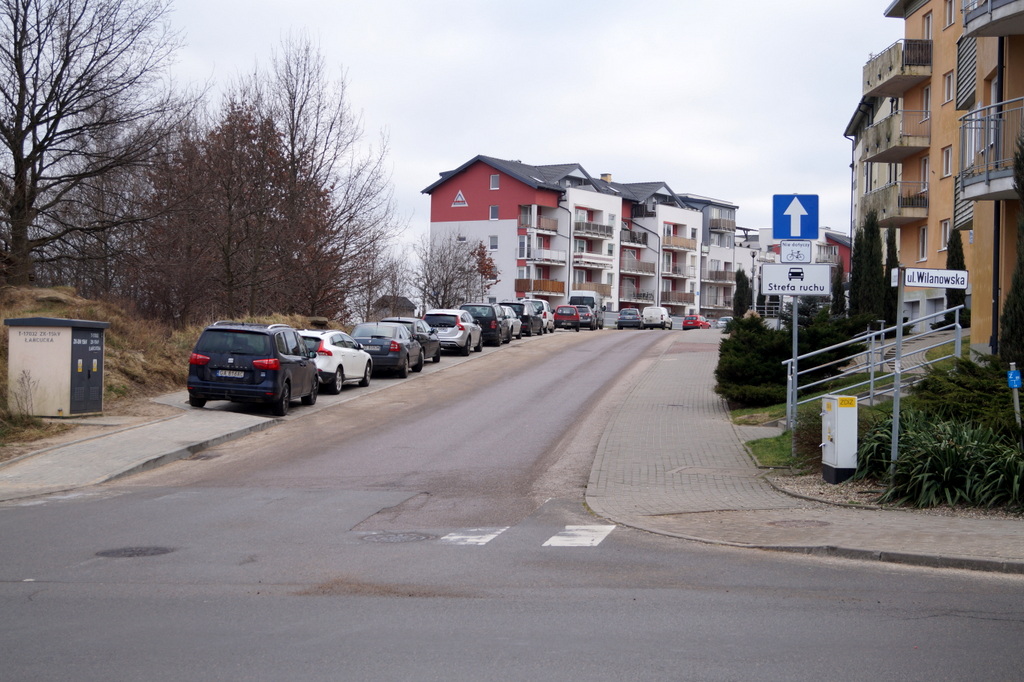 widok na powstałe miejsca parkingowe wzdłuż drogi, widoczne zaparkowane auta, w koło zabudowa mieszklaniowa, widoczneb przejście dla pieszych 